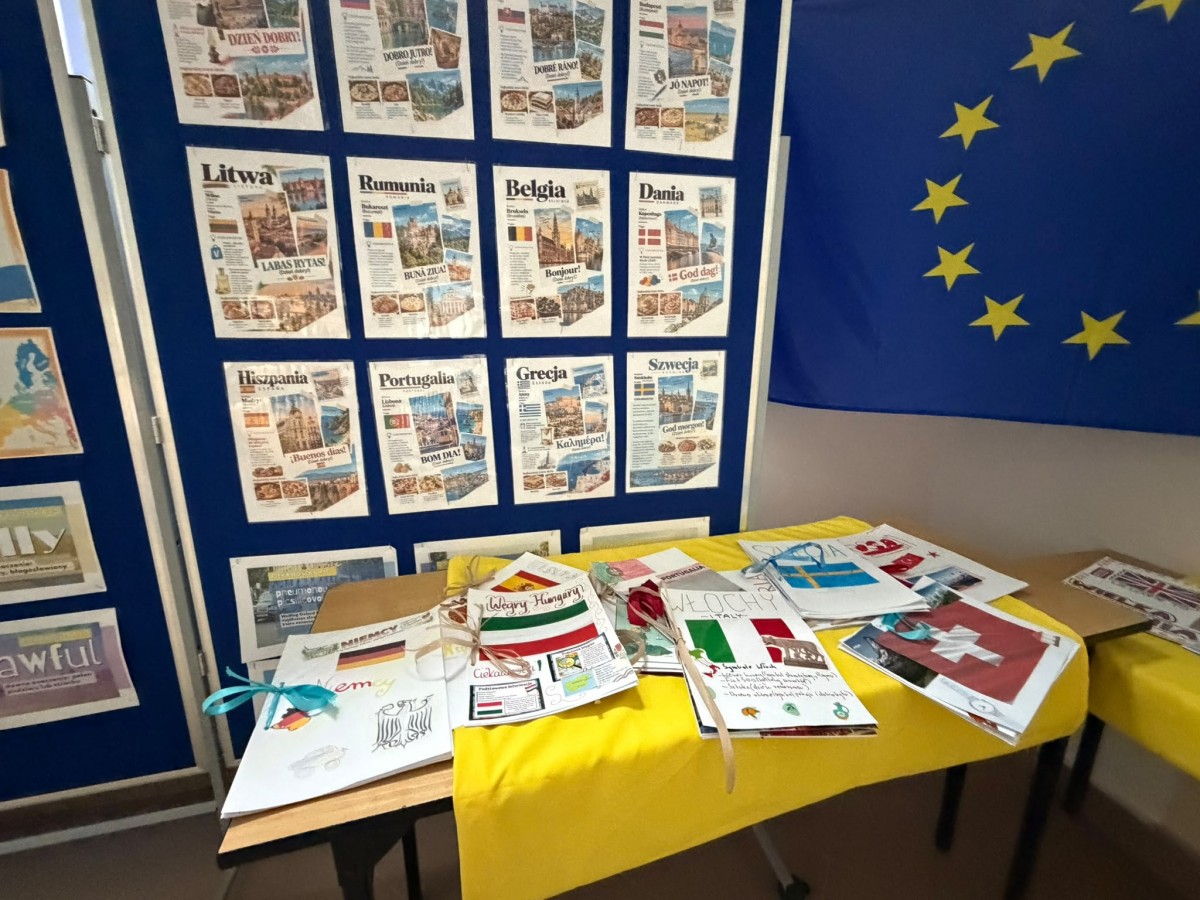 Zdjęcie przedstawia wystawę broszur o krajach europejskich przygotowanych przez uczniów z okazji Europejskiego Dnia Języków Obcych. Prace wyeksponowano na stolikach, a w tle widoczne są tablice z informacjami o państwach Europy oraz flaga Unii Europe