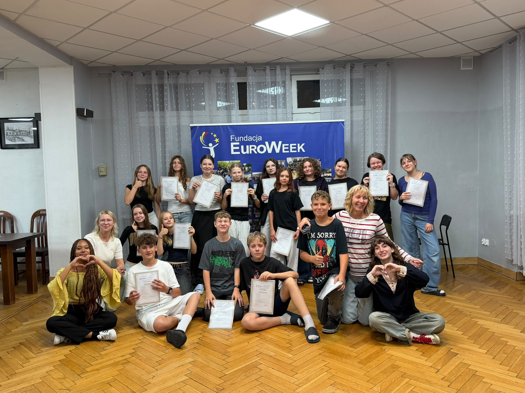 Zdjęcie przedstawia grupę uczniów z klasy 7a wraz z opiekunami i wolontariuszami po zakończeniu warsztaów jezykowych EuroWeek w Kotlinie Kłodzkiej. Uczniowie trzymają certyfikaty, które otrzymali za udział w programie.