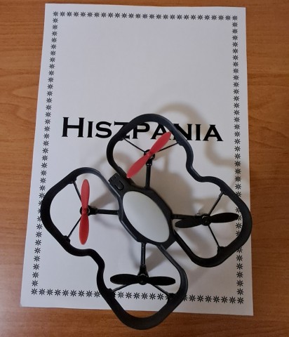 Kartka z napisem Hiszpania, a na niej stojący dron