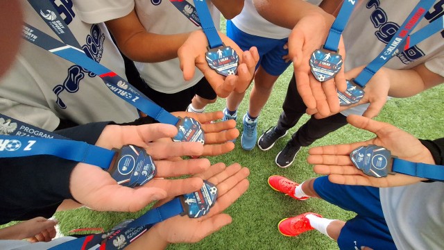 Obraz przedstawia uczniów stojących w kręgu z medalami na rękach