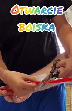 Zdjęcie przedstawia moment przecięcia wstęgi w czasie uroczystości otwarcia boiska sportowego.